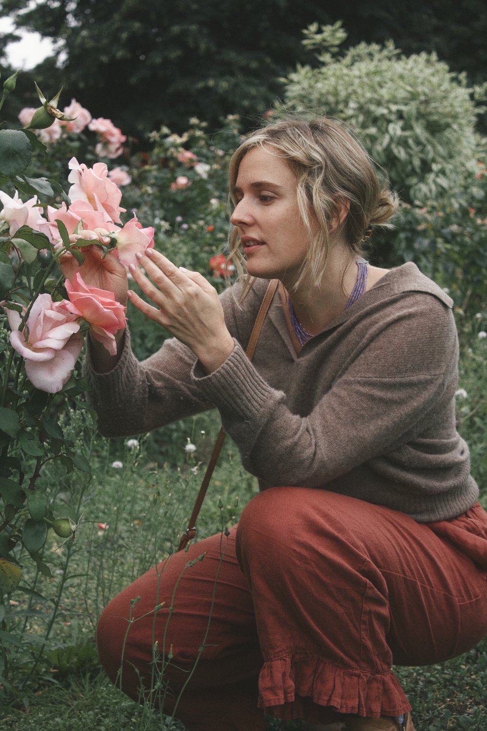 Michaela kneeling in a garden, holding a pink rose